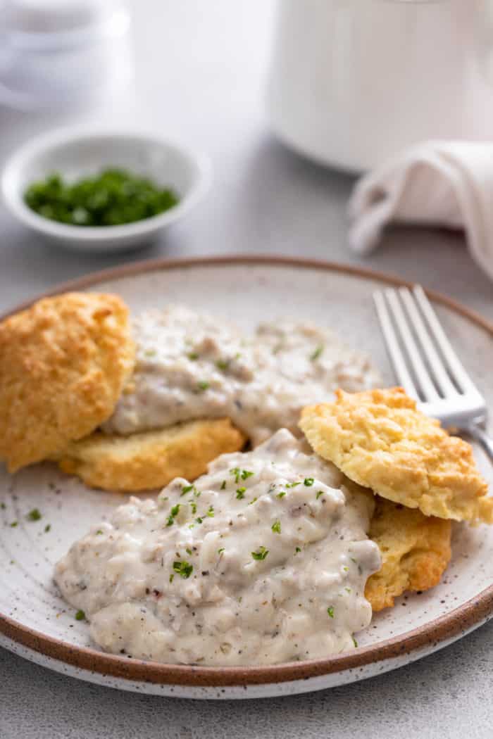 Close up of biscuits topped with sausage gravy on a white and brown plate.
