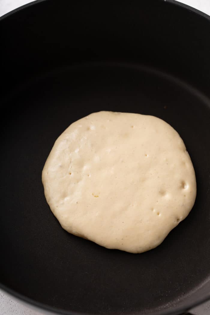 Buttermilk pancake being cooked in a black skillet.
