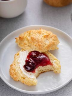 Bite taken from a buttermilk drop biscuit that has been split in half and topped with butter and berry jam.
