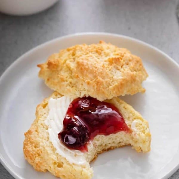 Bite taken from a buttermilk drop biscuit that has been split in half and topped with butter and berry jam.