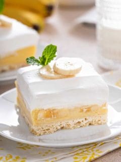 Banana cream bar set on a white plate so you can see the layers of crust, filling, and topping.