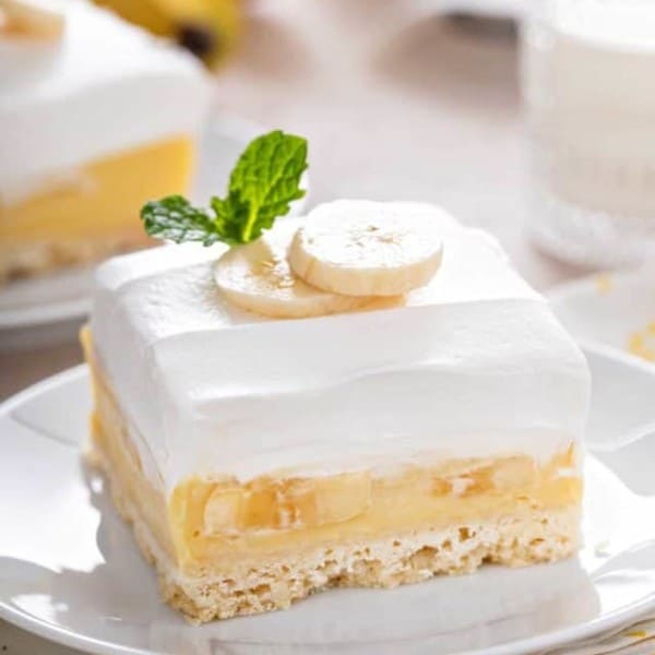 Banana cream bar set on a white plate so you can see the layers of crust, filling, and topping.