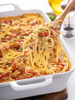 Wooden spoon dishing up a serving of chicken spaghetti casserole out of the baking dish of casserole.