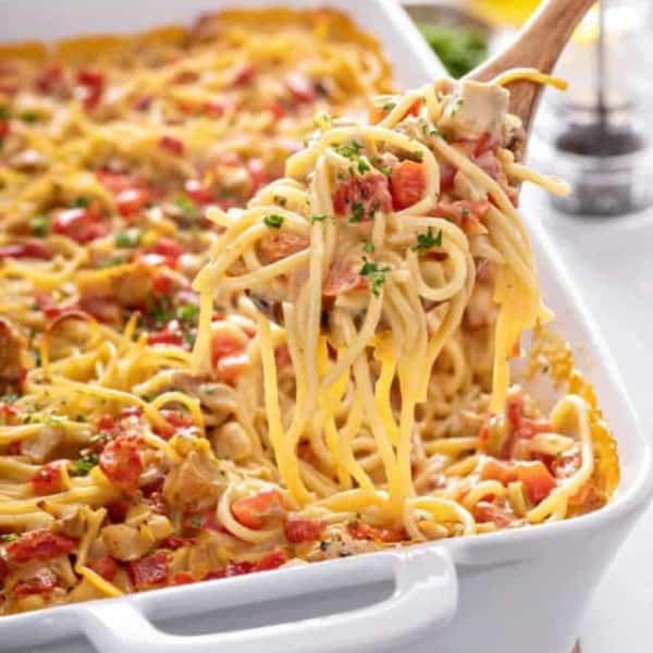 Wooden spoon dishing up a serving of chicken spaghetti casserole out of the baking dish of casserole.