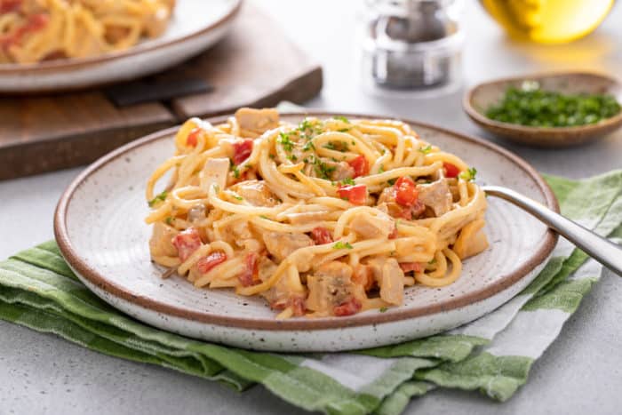 Chicken spaghetti casserole next to a fork on a ceramic plate. A second plate is visible in the background.