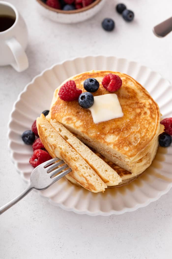 Overhead view of plated buttermilk pancakes with a bite cut off and on the fork that is next to the pancakes.