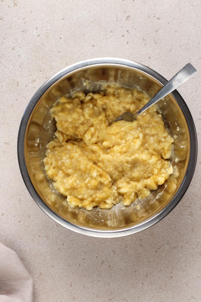 Mashed ripe bananas in a metal mixing bowl.