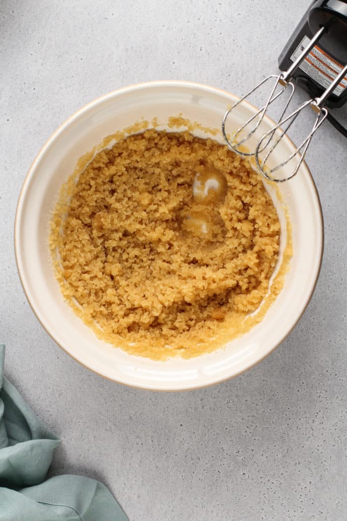 Brown butter and sugar beaten together in a ceramic mixing bowl.