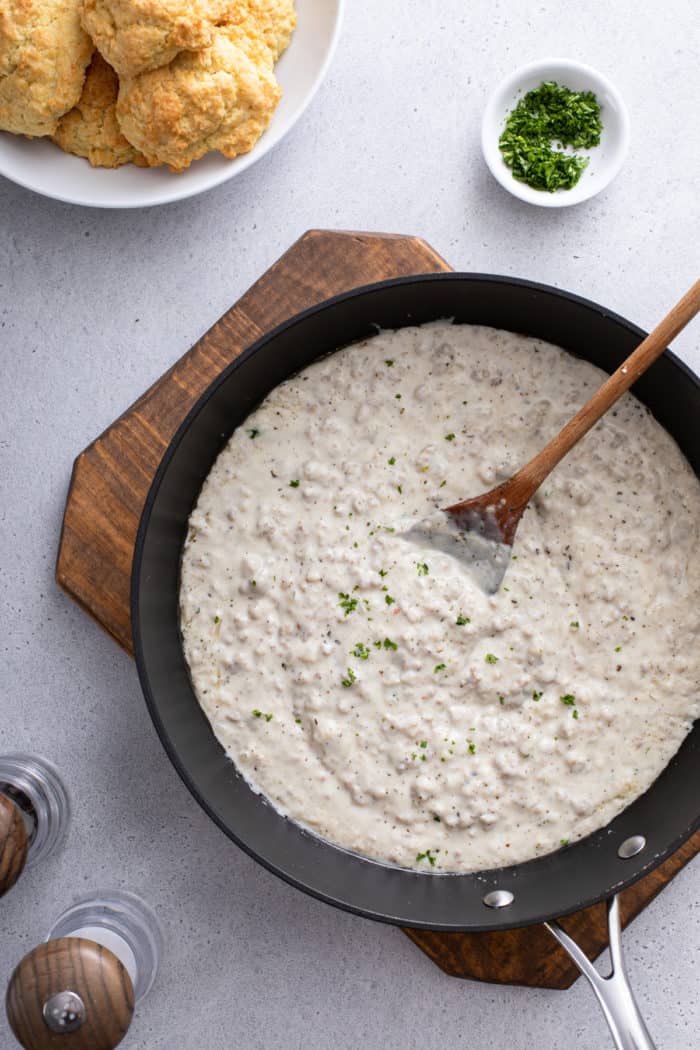 Overhead view of sausage gravy in a black skillet set on a wooden board.