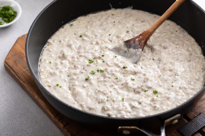 Black skillet filled with sausage gravy set on a wooden trivet.