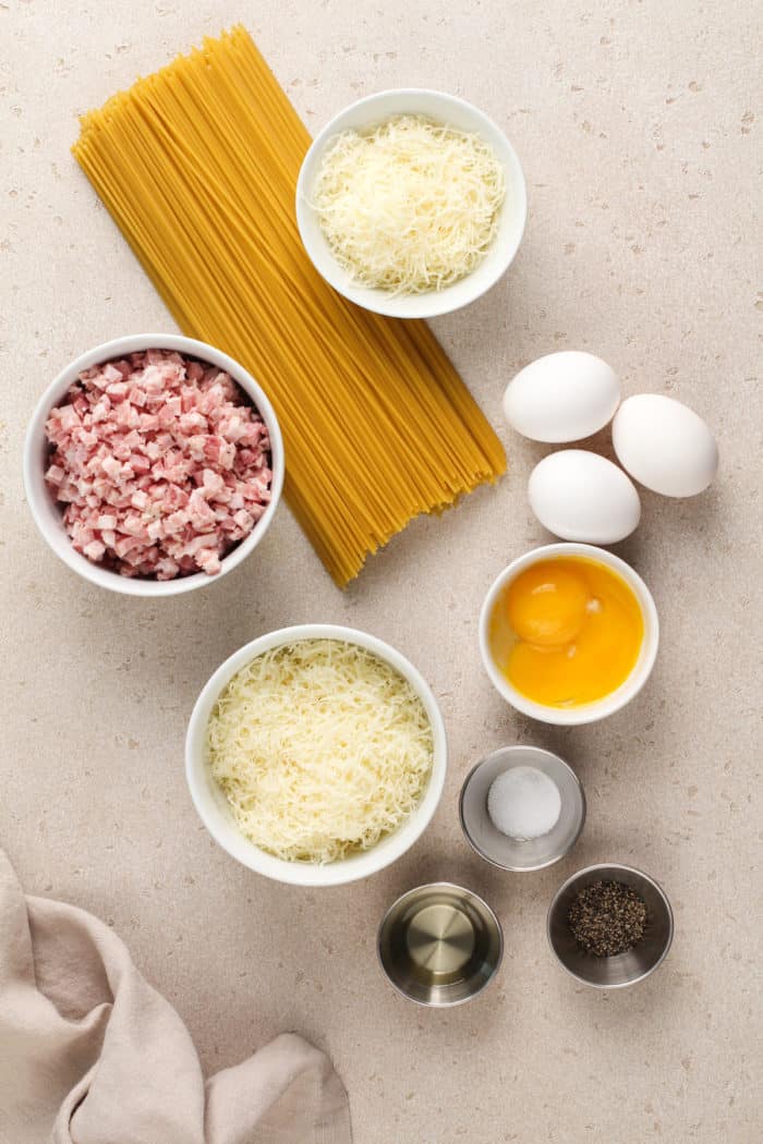 Ingredients for pasta carbonara arranged on a beige countertop.