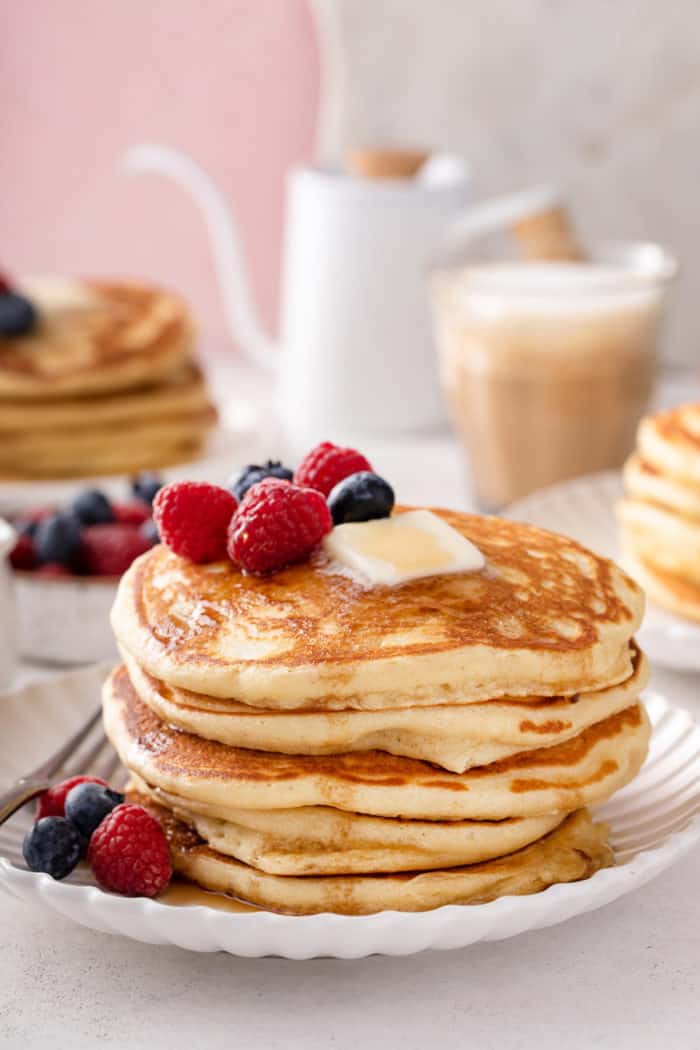 Several buttermilk pancakes stacked on a white plate and garnished with fresh berries.