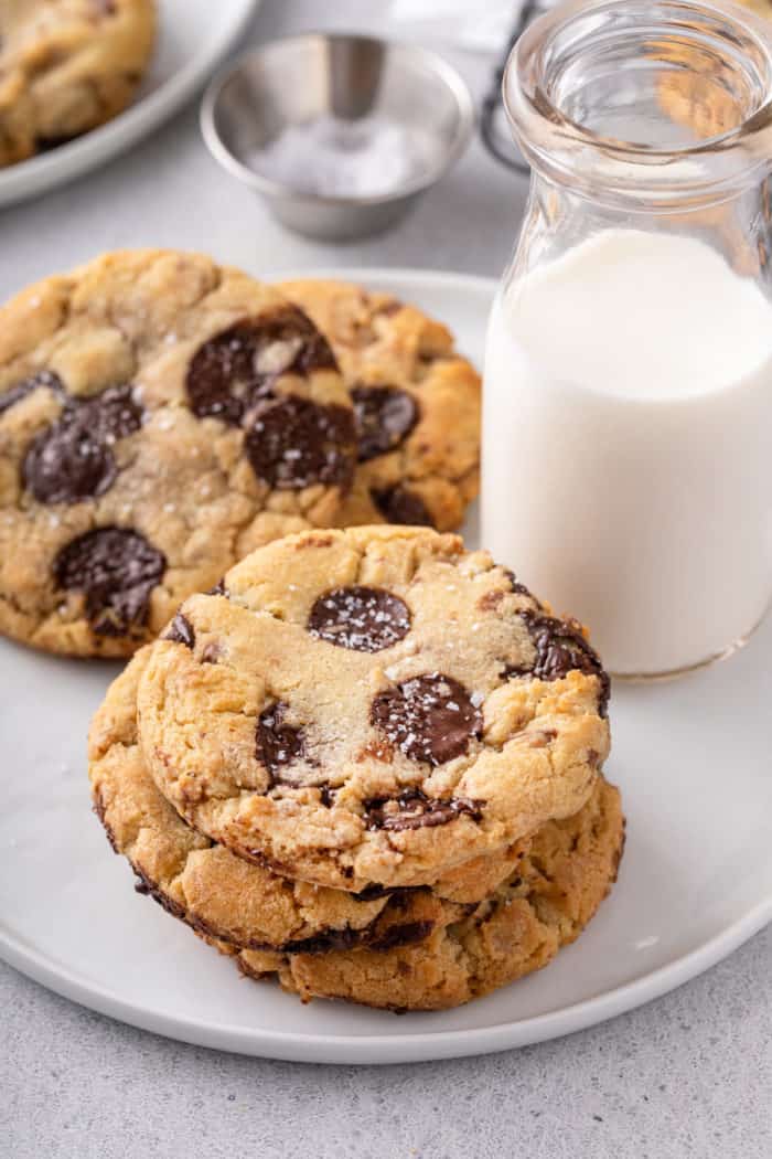 Chocolate chip cookies with brown butter and toffee on a white plate next to a glass of milk.