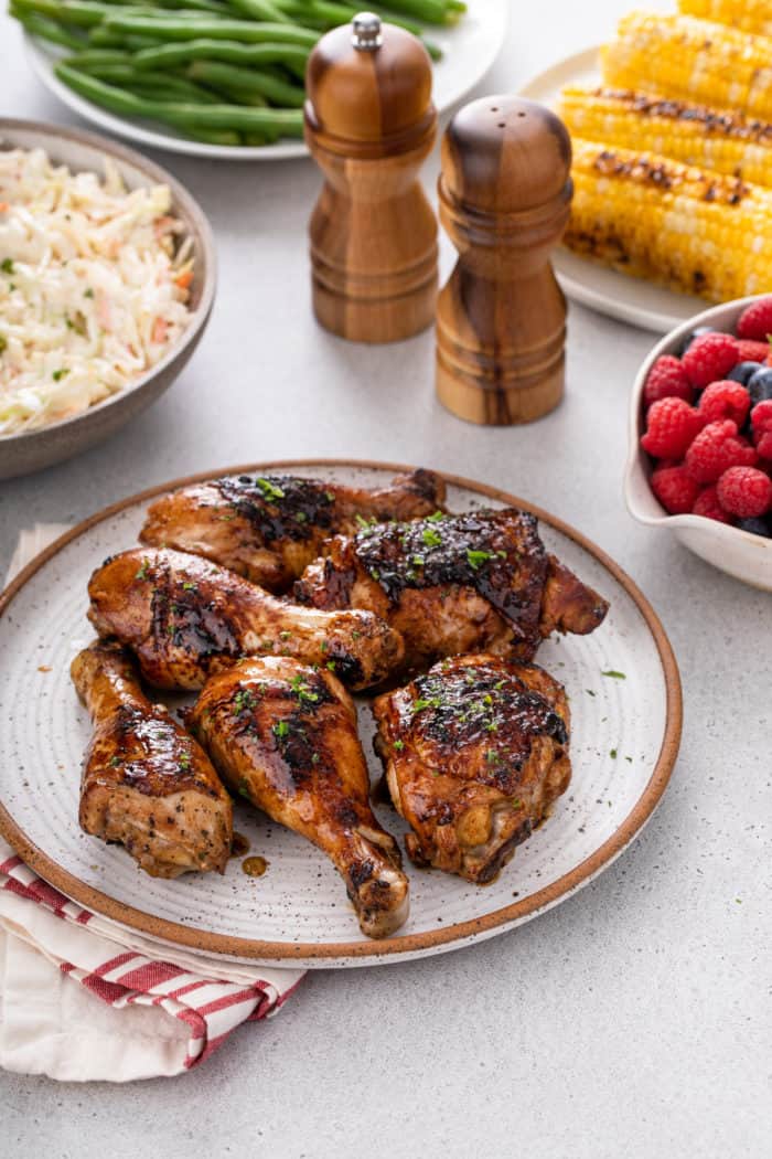 Stoneware plate piled with pieces of grilled chicken. Plates of side dishes are visible in the background.