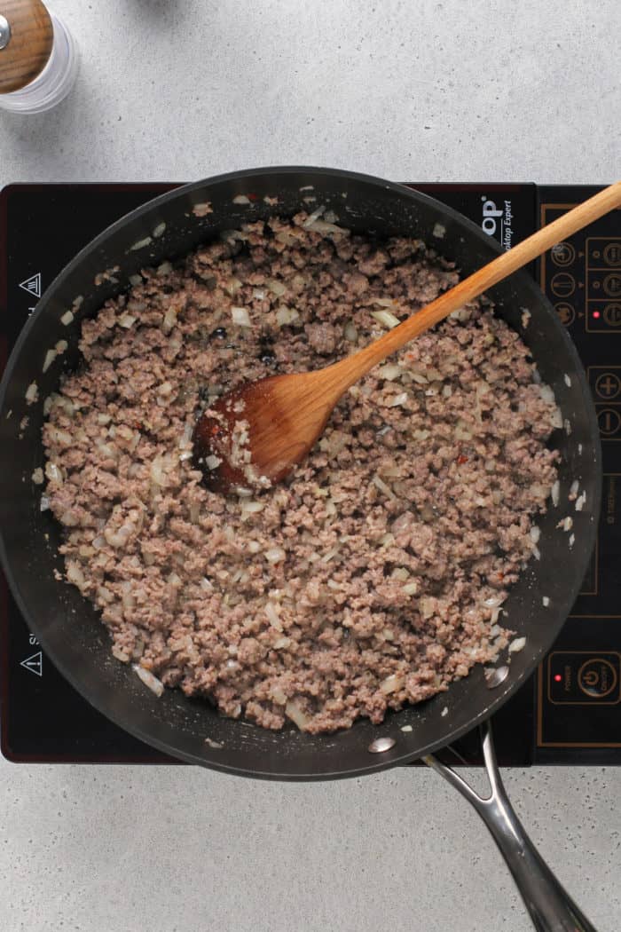 Browned sausage with cooked onion and garlic in a black skillet on an induction burner.