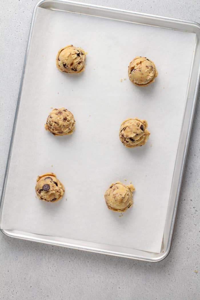 Six balls of chocolate chip cookie dough with brown butter and toffee portioned onto a parchment-lined baking sheet.