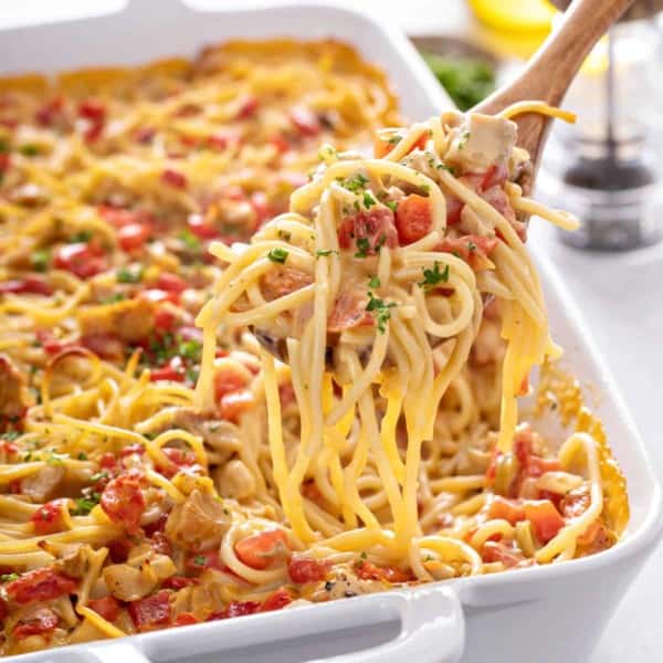 Spoonful of chicken spaghetti being lifted up from the baking dish.