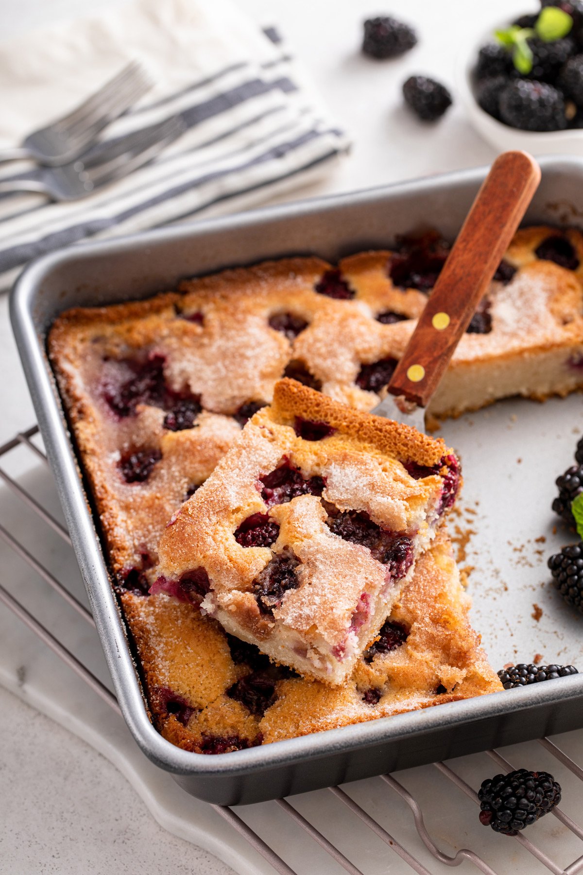 A slice of blackberry cobbler on a cake server over the pan of easy blackberry cobbler.