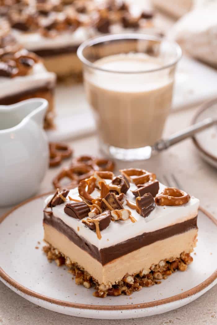 Side of of a slice of peanut butter pretzel dessert on a speckled plate, showing the layers of the piece of dessert.