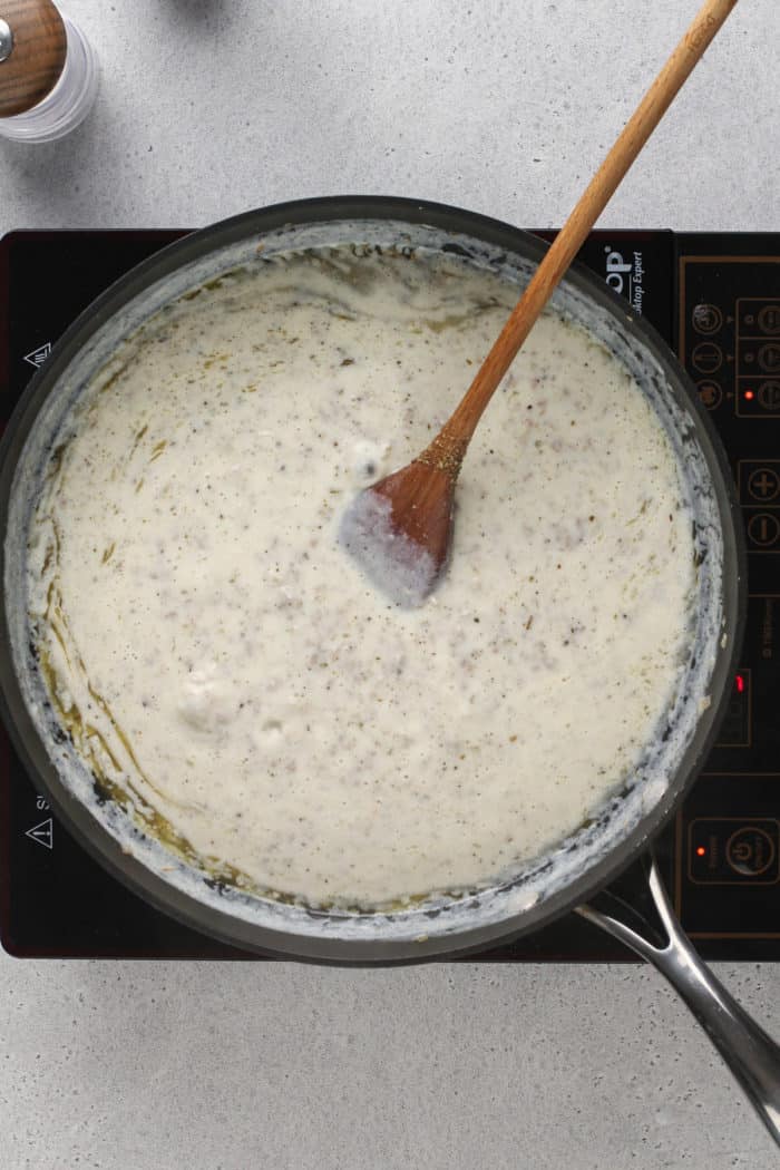 Sausage gravy simmering in a black skillet set on an induction burner.