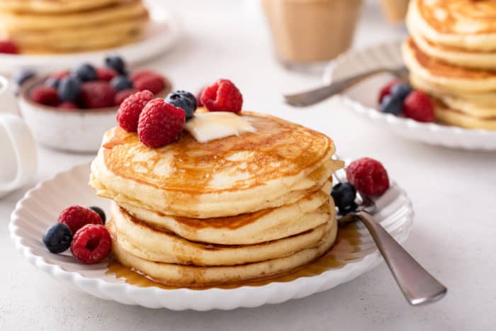 Stack of buttermilk pancakes topped with butter, fresh berries, and syrup on a white plate.
