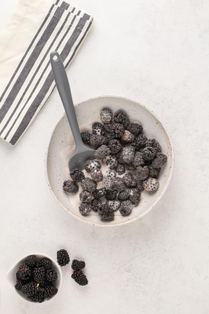 Fresh blackberries stirred together with sugar in a white mixing bowl.