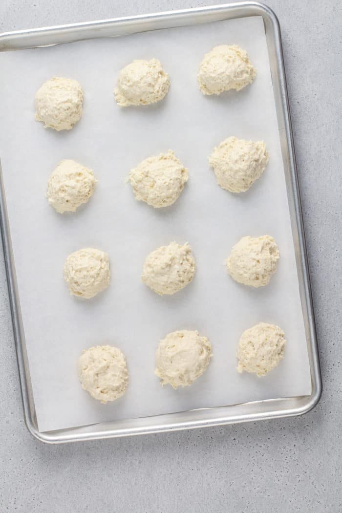 Unbaked buttermilk drop biscuits on a parchment-lined baking sheet, ready to go in the oven.