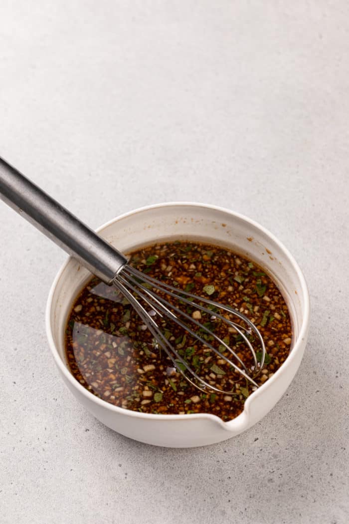 Whisking together ingredients for the best grilled chicken marinade in a white bowl.