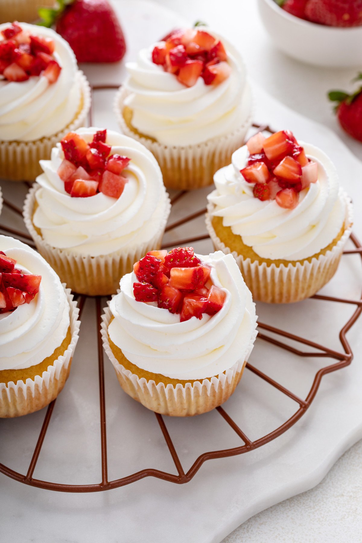 Several strawberry shortcake cupcakes arranged on a round wire rack.