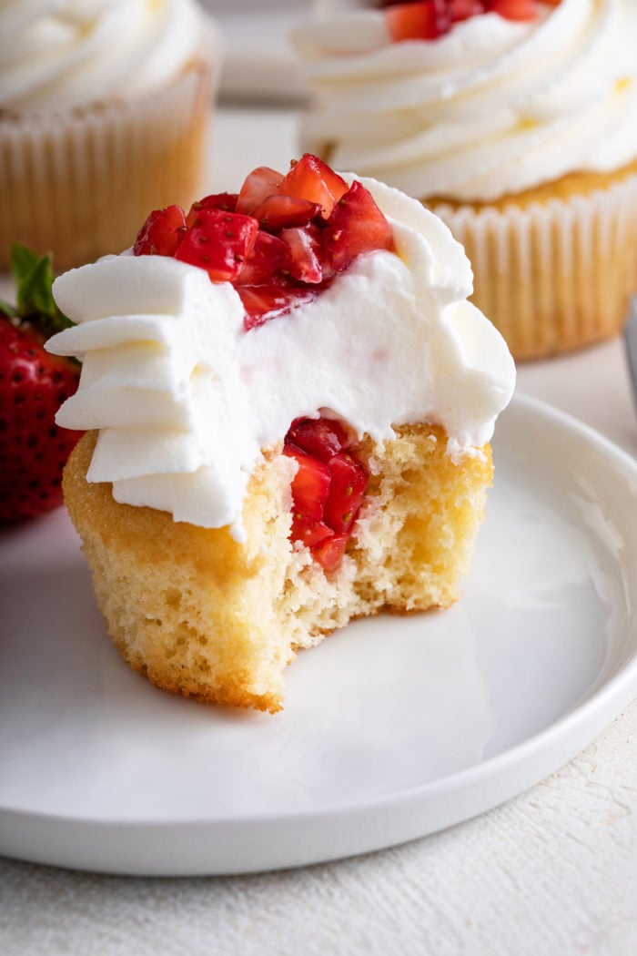 Half of a strawberry shortcake cupcake on a white plate, showing the diced strawberries in the center.