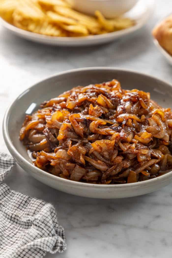 Gray bowl filled with caramelized onions, set on a marble countertop.