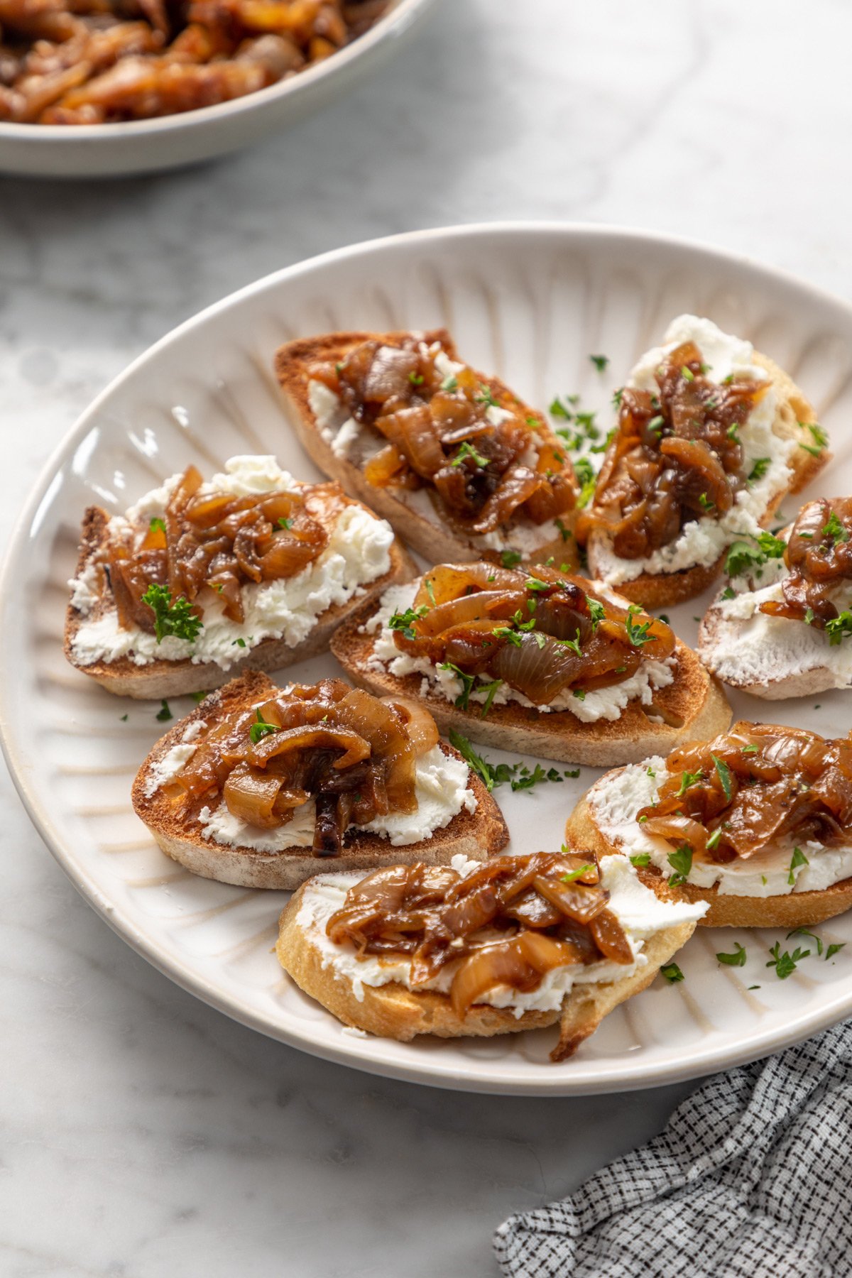 White platter filled with crostini topped with goat cheese and caramelized onions.