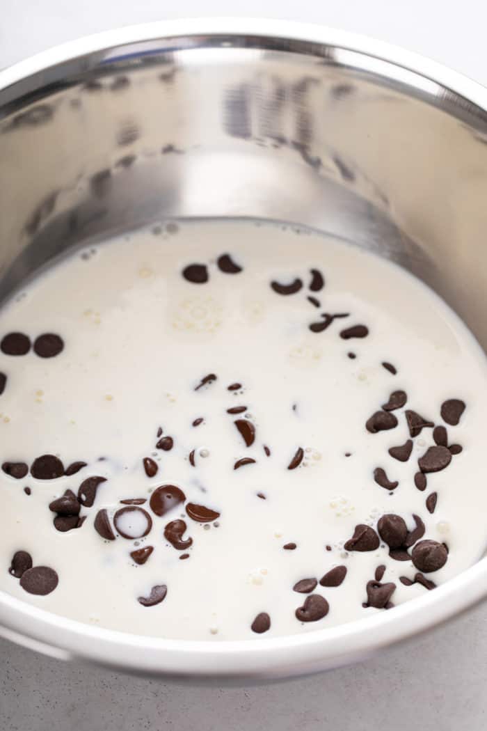 Heavy cream and chocolate chips in a metal mixing bowl.