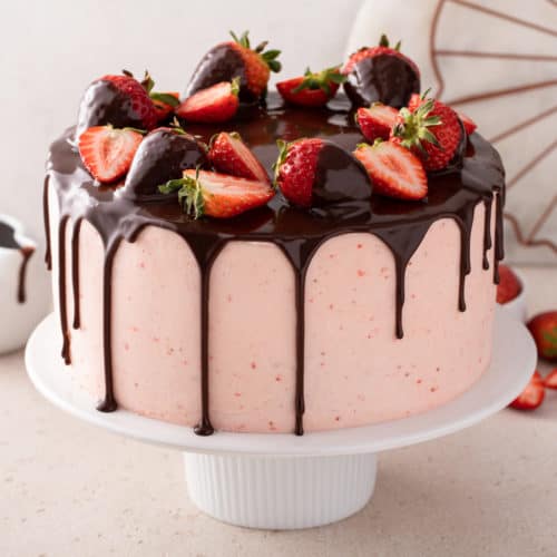 Ganache-topped chocolate strawberry cake on a white cake stand.