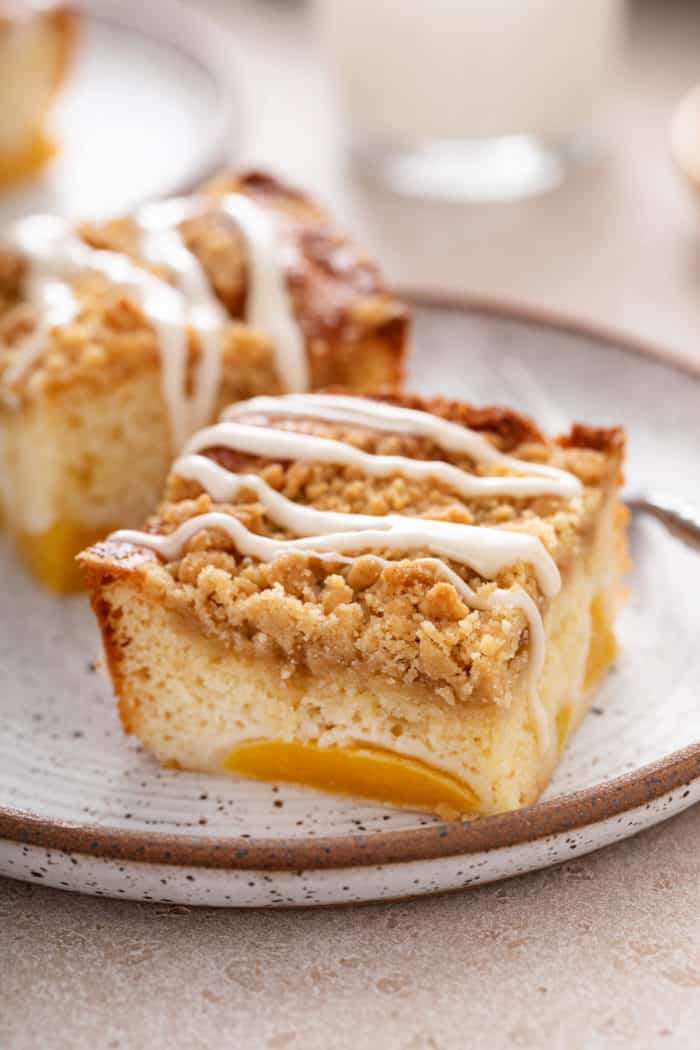 Two slices of easy peach coffee cake on a speckled plate. The bottom of a glass of milk is faintly visible in the background.