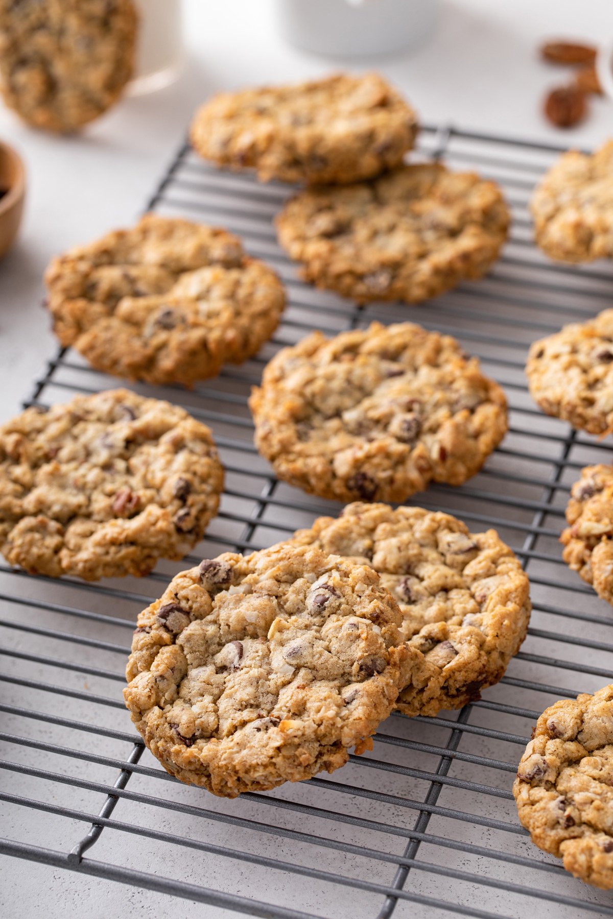 Several cowboy cookies scattered in a wire cooling rack set on a countertop.