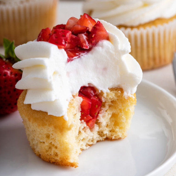 Half of a strawberry shortcake cupcake on a white plate, showing the diced strawberries in the center.