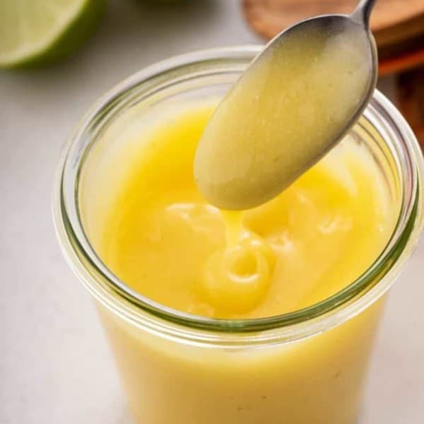 Spoon drizzling lime curd back into a glass jar of the curd.