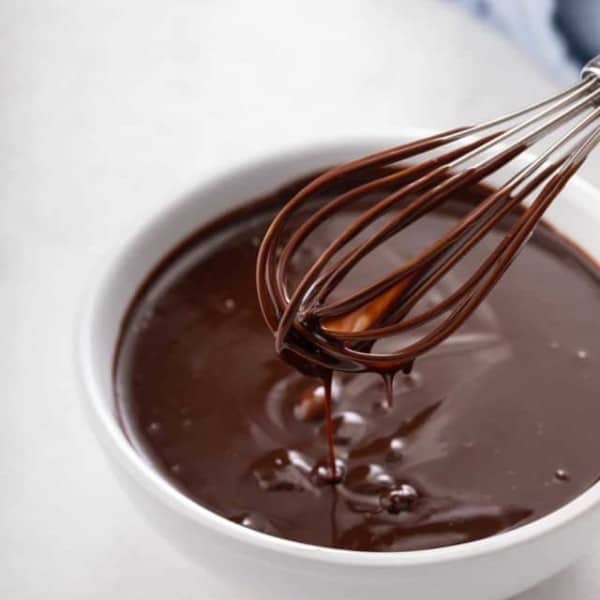 Chocolate ganache being whisked in a small white bowl.