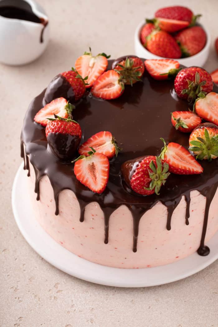 Strawberry-frosted chocolate cake topped with chocolate ganache and fresh strawberries set on a white plate.