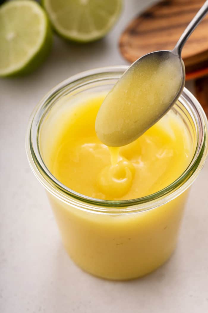 Spoon drizzling lime curd back into a glass jar of the curd.