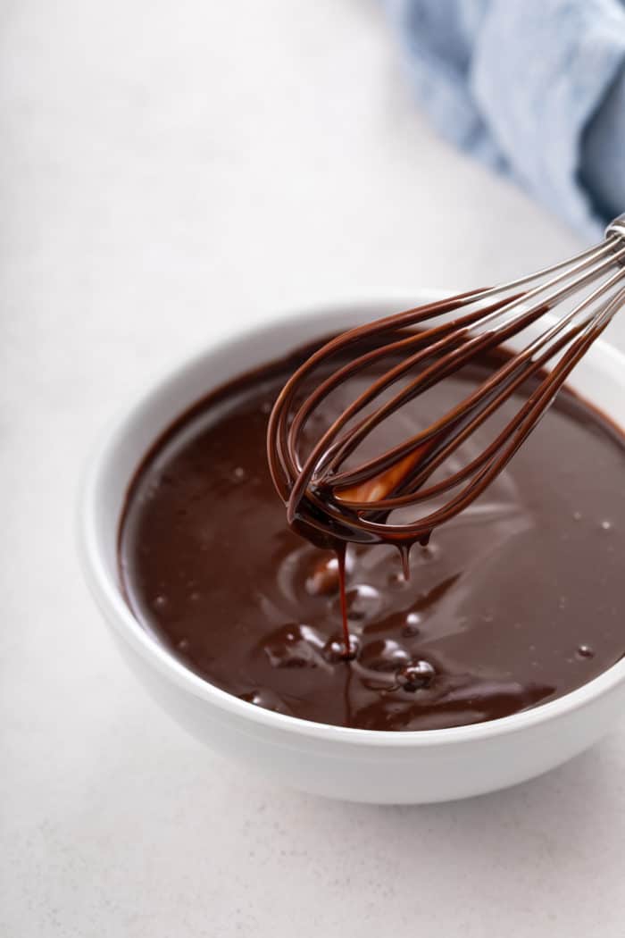 Chocolate ganache being whisked in a small white bowl.