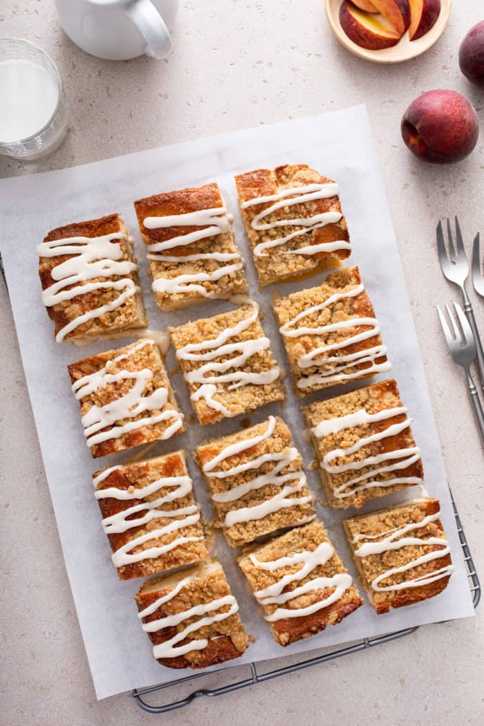 Iced and sliced easy peach coffee cake set on a piece of parchment paper.