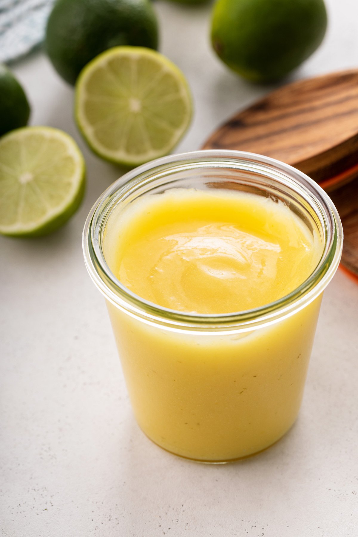 Glass jar filled with lime curd. Fresh limes are visible in the background.