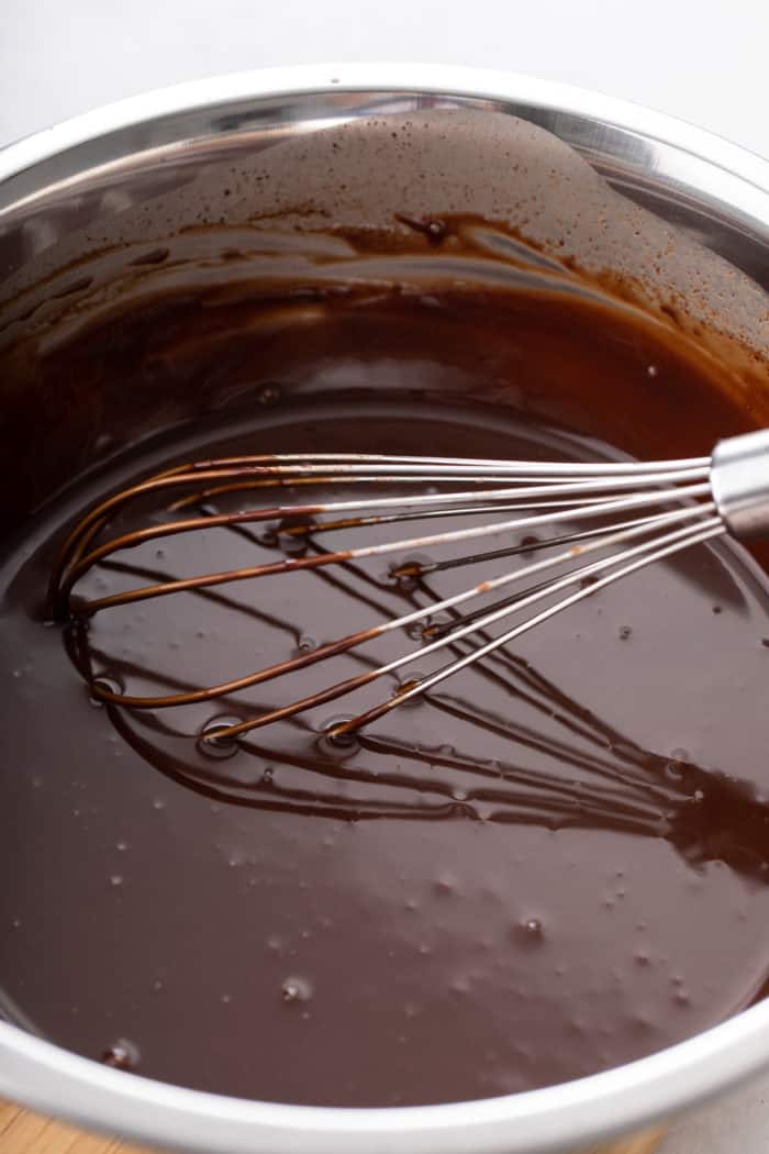 Chocolate ganache being whisked in a metal mixing bowl.