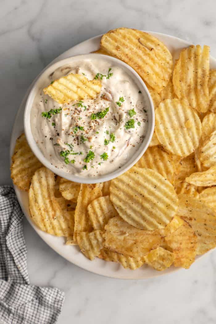 Bowl of caramelized onion dip on a plate next to ruffled potato chips.