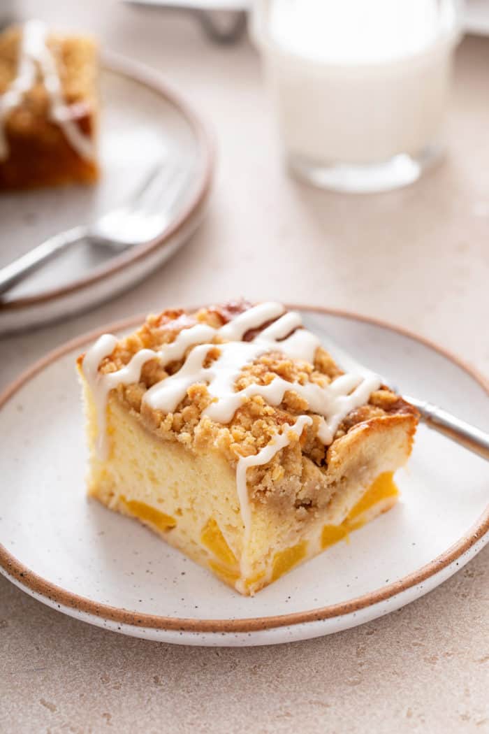 Slice of easy peach coffee cake on a speckled plate. A glass of milk is visible in the background.