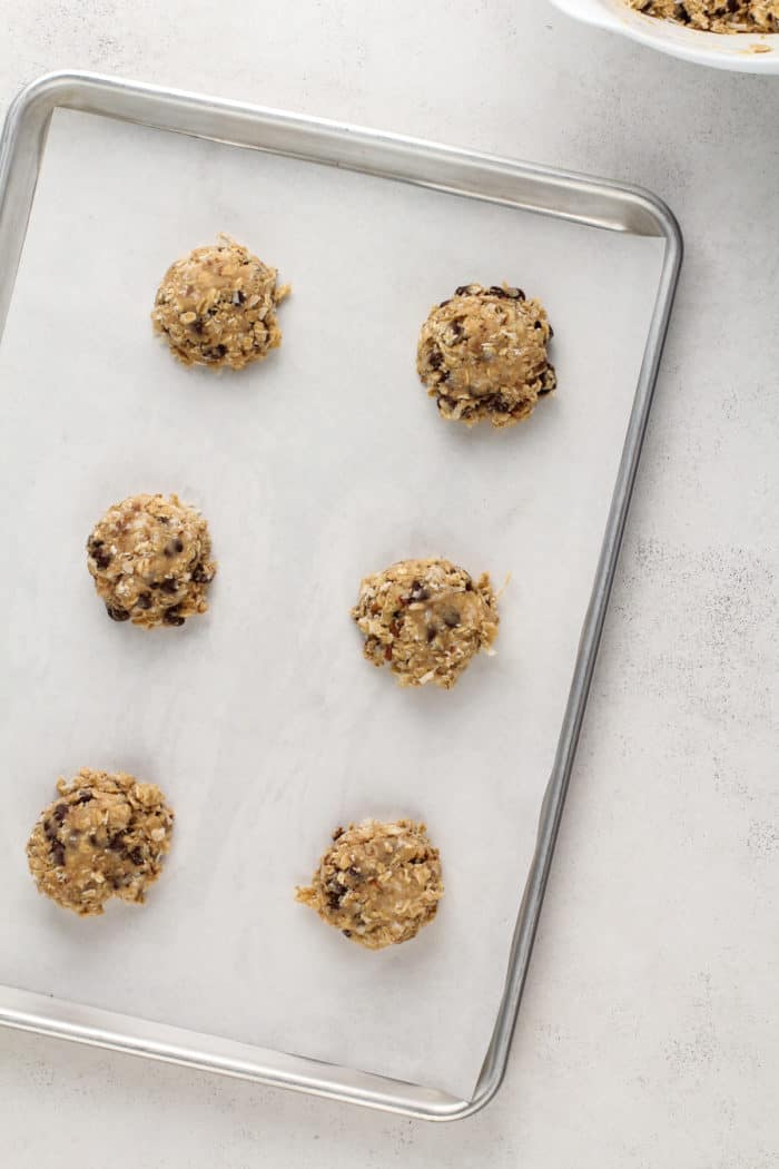 Three large cookie dough balls on a parchment-lined baking sheet, ready to go in the oven.