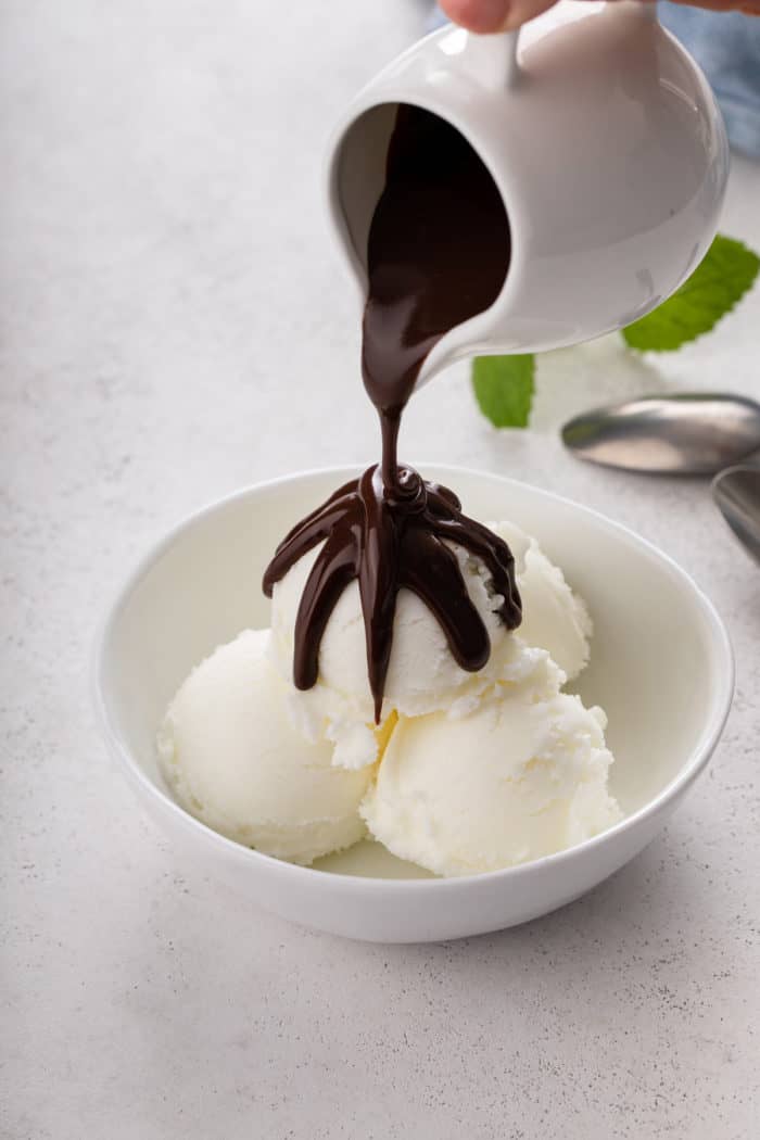 Chocolate ganache being poured over vanilla ice cream in a white bowl.