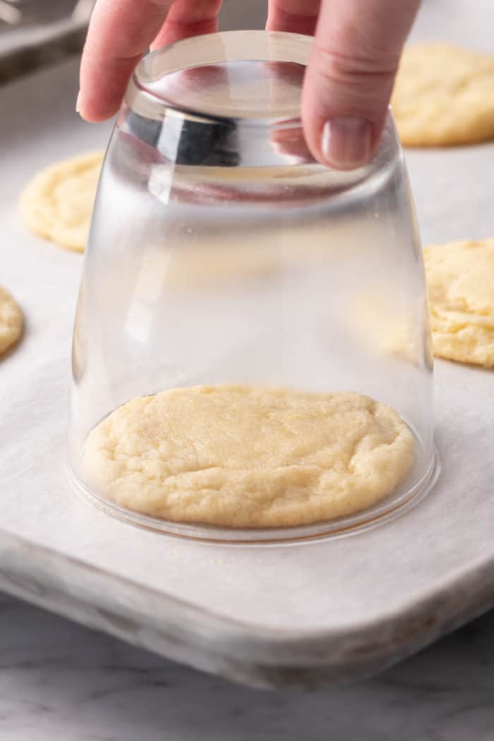 Glass shaping a sugar cookie on a parchment-lined baking sheet.